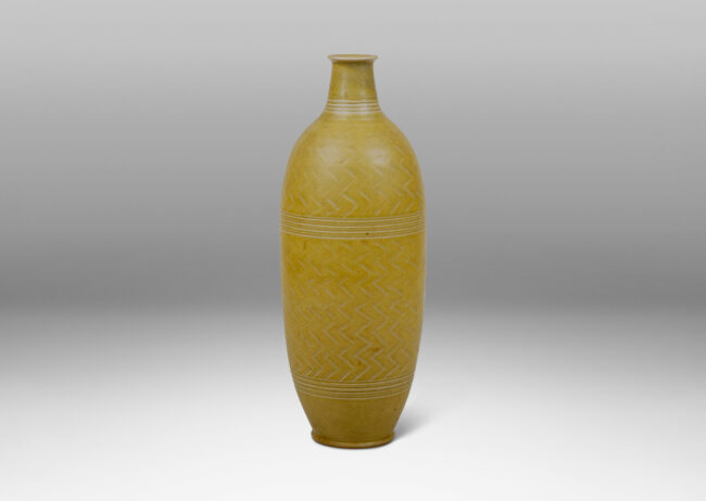 Gallery BAC elongated and tapered bottle form with a short neck and delicate unfolded mouth, carved with a herringbone design