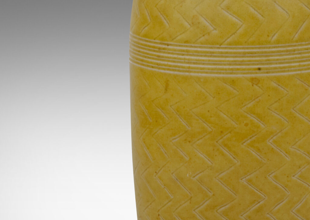 Gallery BAC elongated and tapered bottle form with a short neck and delicate unfolded mouth, carved with a herringbone design