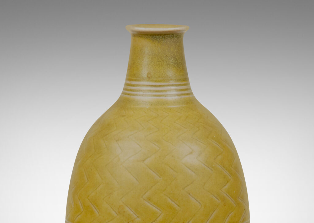 Gallery BAC elongated and tapered bottle form with a short neck and delicate unfolded mouth, carved with a herringbone design