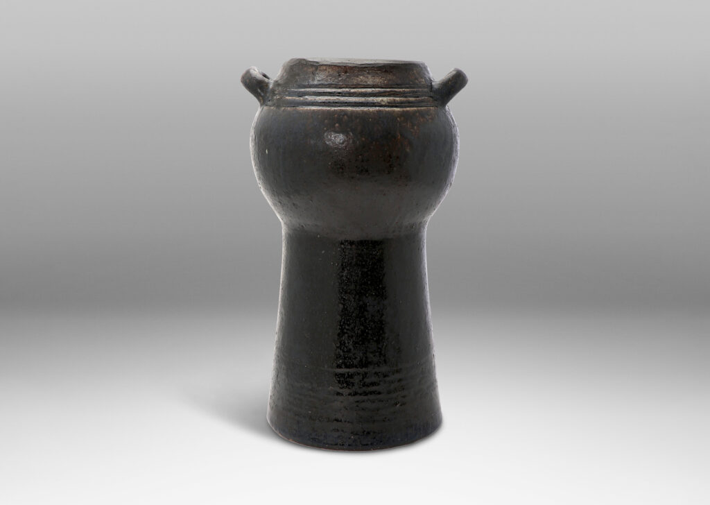 Gallery BAC spherical form with two handles on an engaged conical stand; hand-thrown stoneware with a moody black/blue/brown glaze