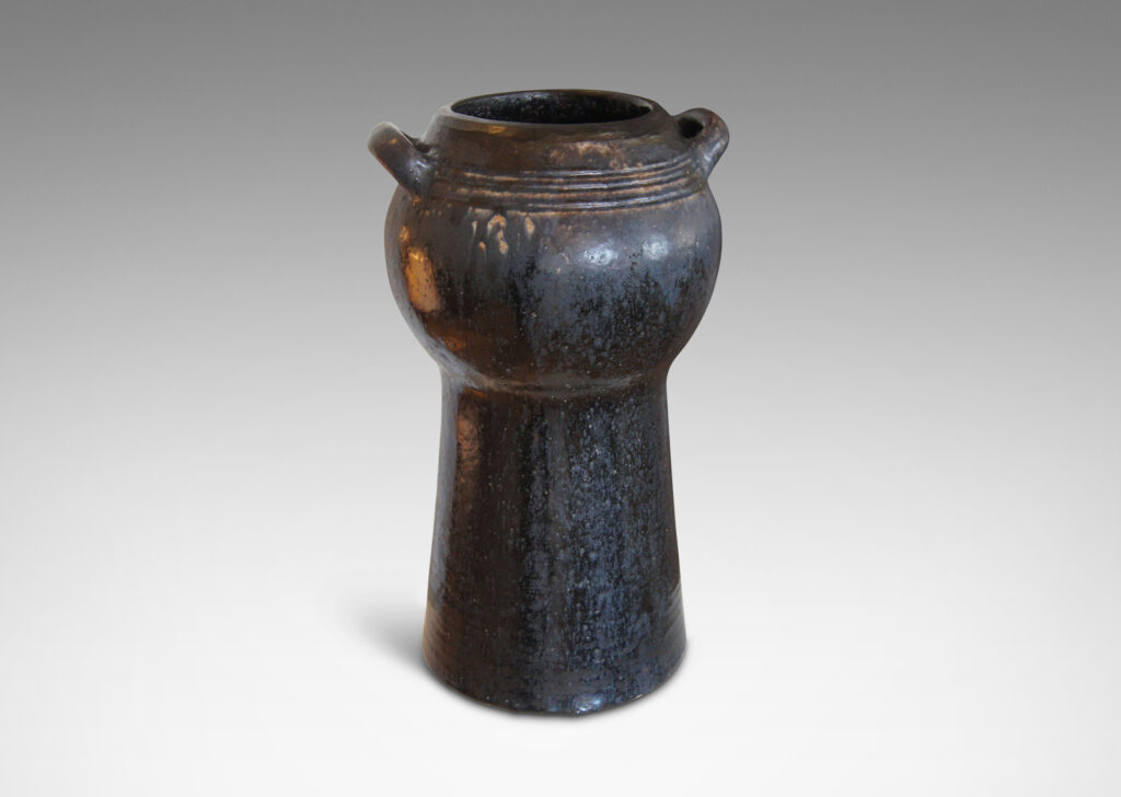 Gallery BAC spherical form with two handles on an engaged conical stand; hand-thrown stoneware with a moody black/blue/brown glaze