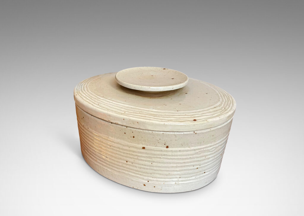 Gallery BAC oval form, with carved ridges encircling the box and bordering the edges of the lid; hand-crafted in a speckled pale gray stone ware