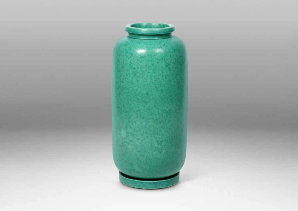 Gallery BAC cylindrical form with rounded ends, notched neck/mouth and tray stand in a mottled blue-green copper oxide glaze