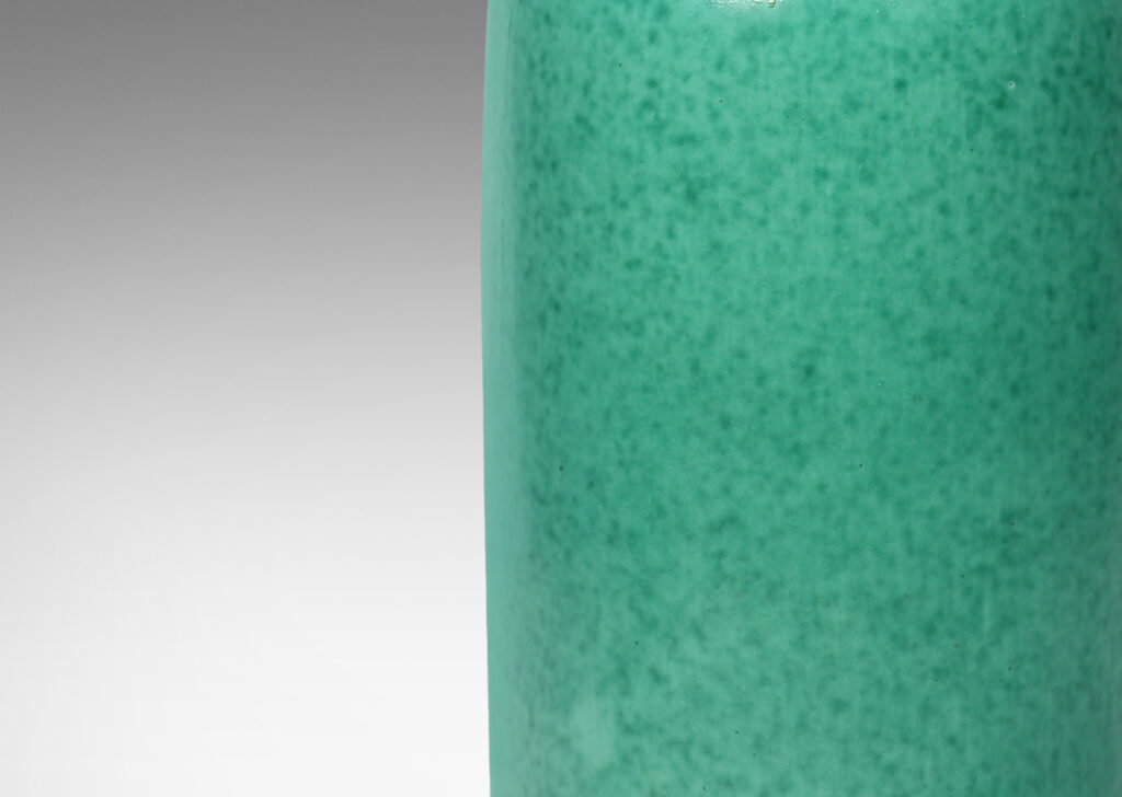 Gallery BAC cylindrical form with rounded ends, notched neck/mouth and tray stand in a mottled blue-green copper oxide glaze