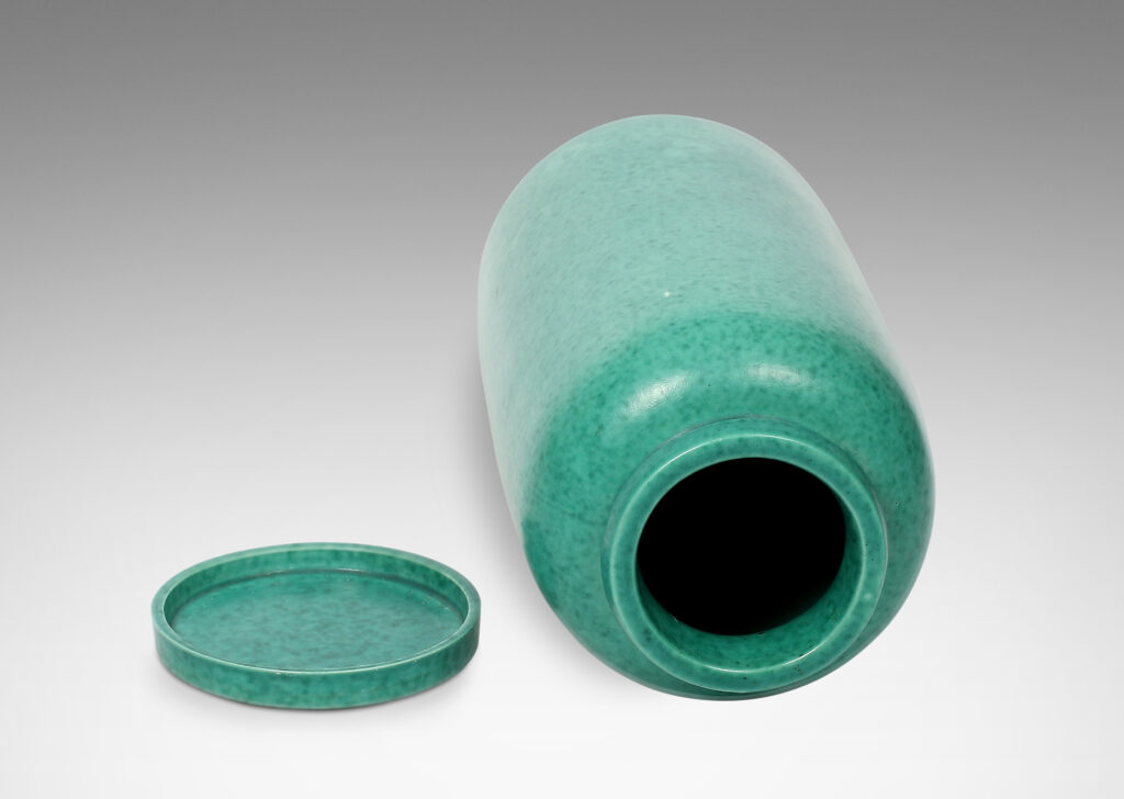 Gallery BAC cylindrical form with rounded ends, notched neck/mouth and tray stand in a mottled blue-green copper oxide glaze