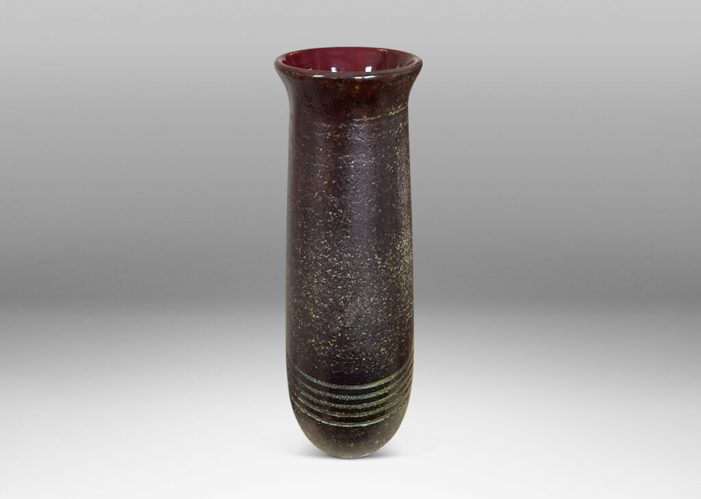 Gallery BAC elongated textured form with flared mouth and carved banding glazed in black over pale green-gray on the outside and burgundy inside