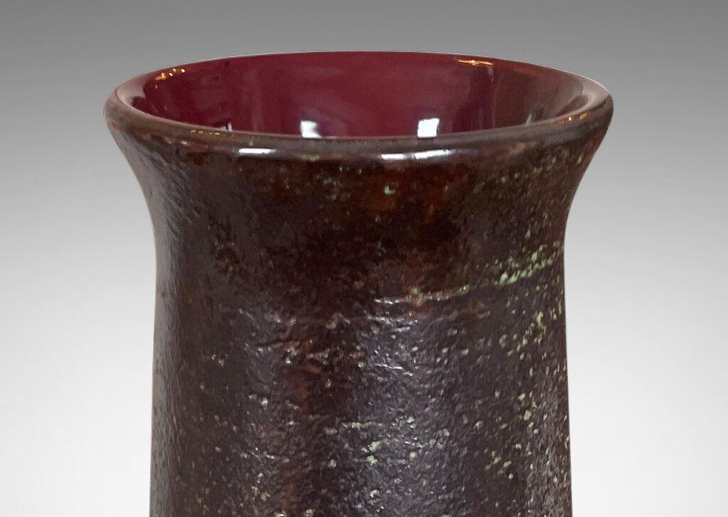 Gallery BAC elongated textured form with flared mouth and carved banding glazed in black over pale green-gray on the outside and burgundy inside