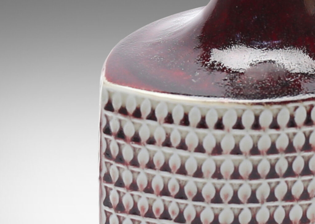 Gallery BAC football/ovoid drum form with registers of leaf motifs in relief and tall neck in a marvelous oxblood glaze