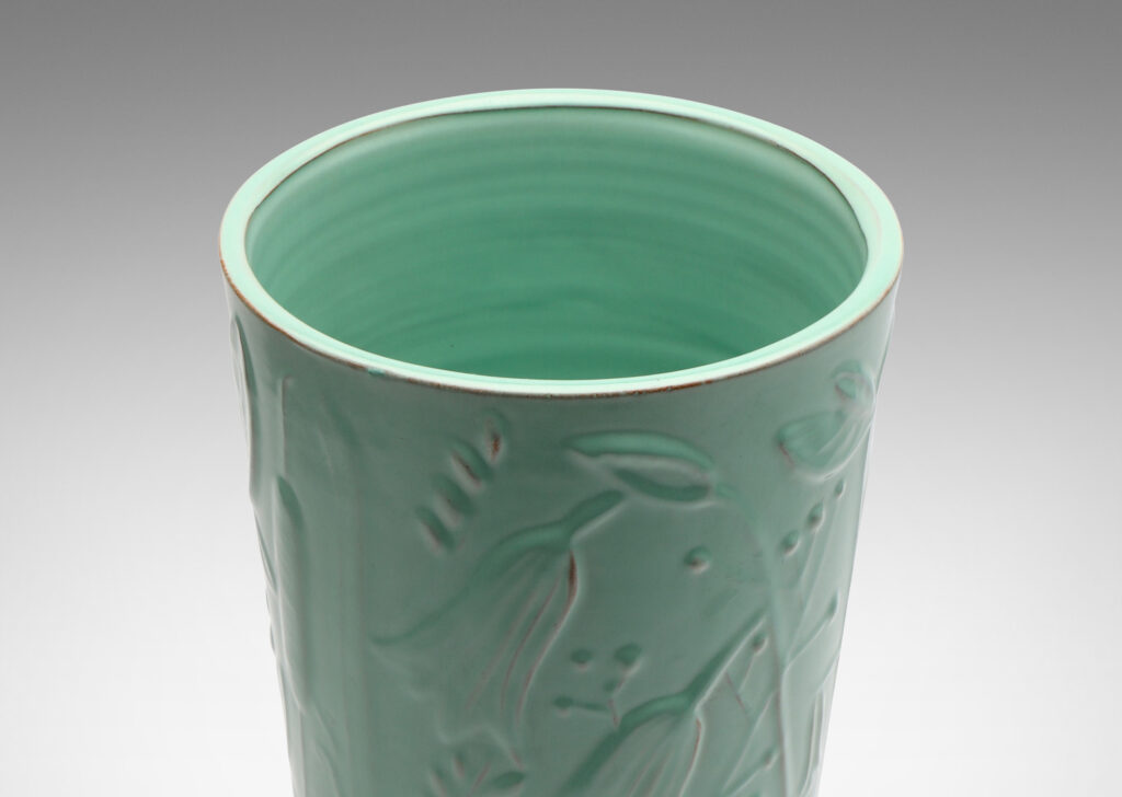 Gallery BAC tall cylindrical form surrounded in floral reliefs and glazed in an eggshell finish celadon