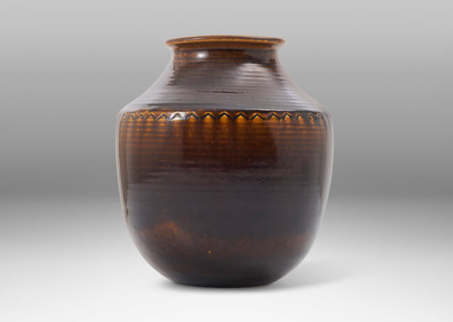 Gallery BAC wide half-spherical form with cove neck and wide mouth with squared lip, with turning grooves and carved chevrons catching a flowing brown glaze