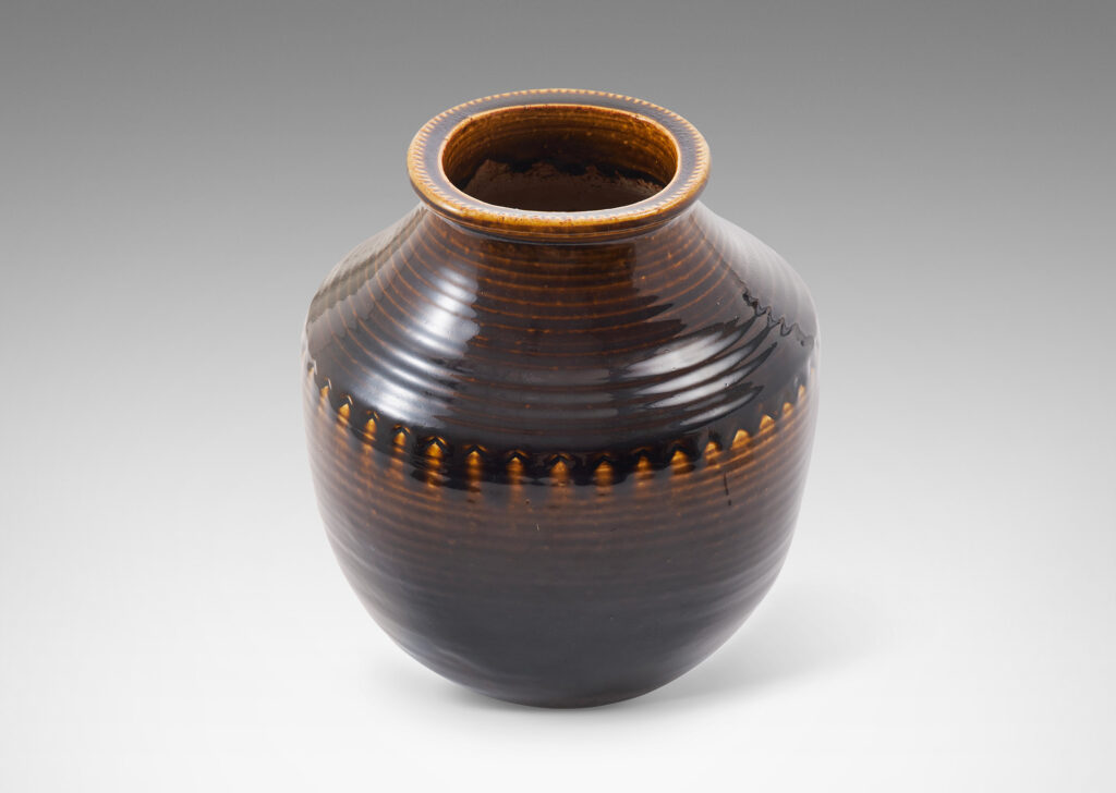 Gallery BAC wide half-spherical form with cove neck and wide mouth with squared lip, with turning grooves and carved chevrons catching a flowing brown glaze