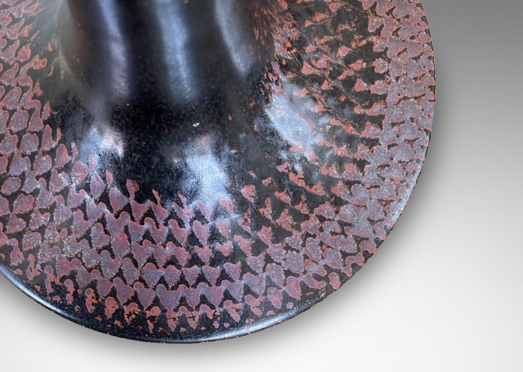 Gallery BAC wide drum form with tall sprouting neck and impressed pattern of radial chevrons, glazed in black with touches of oxblood-rust