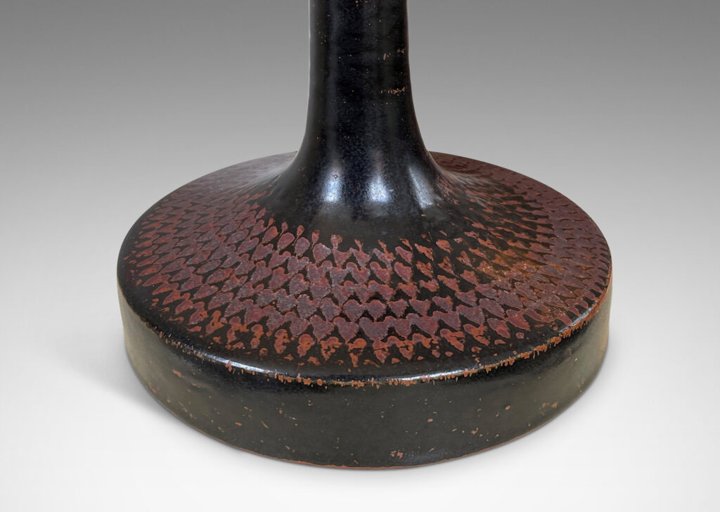 Gallery BAC wide drum form with tall sprouting neck and impressed pattern of radial chevrons, glazed in black with touches of oxblood-rust