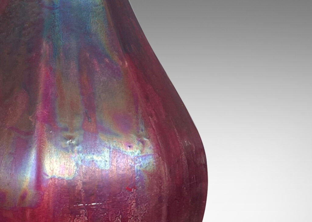 Gallery BAC octagonally-faceted decanter form with attenuated neck, glazed in berry red and teal luster