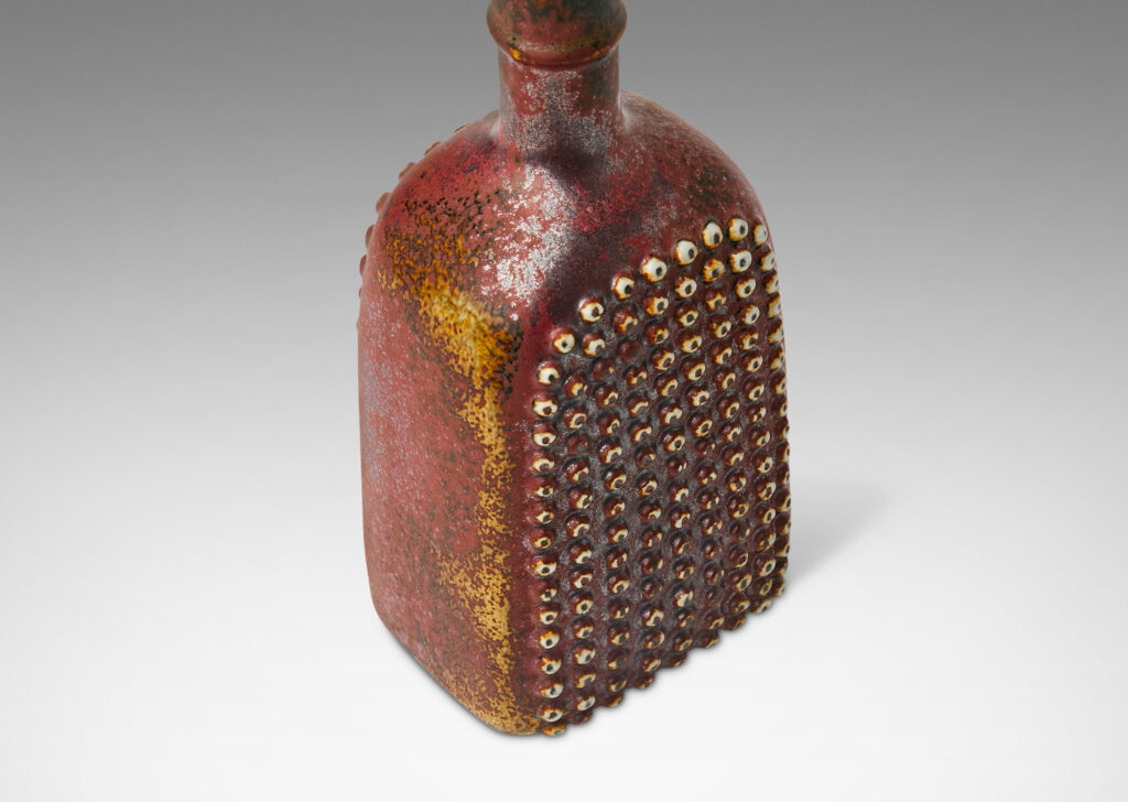 Gallery BAC bottle-like form with grids of cleats in reliefs on two sides and an uncommon dappled oxblood glaze with black accents