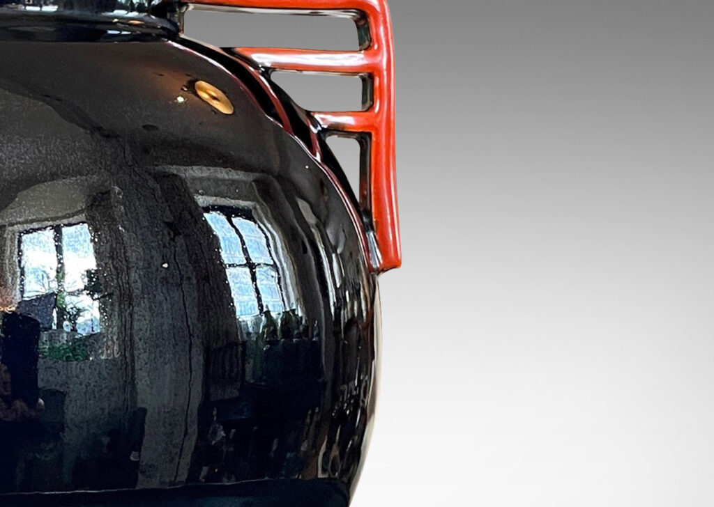 Gallery BAC globe form glazed in a gloss black with vermillion bracket handles