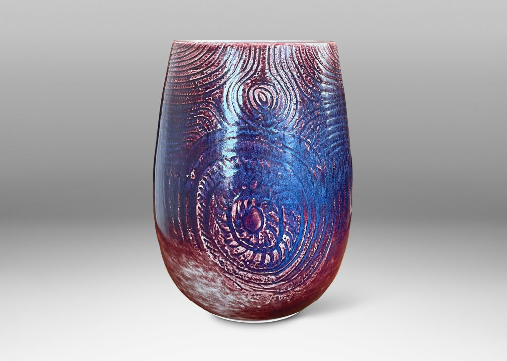 Gallery BAC ovoid form with wide mouth and carved organic coiling and radiating linear pattern, glazed in oxblood with hints of purple and pale gray