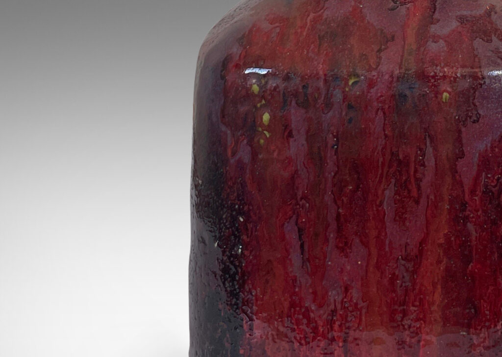 Gallery BAC square bottle-like form with rows of carved circle motifs and sprouting neck, glazed in a thick flowing burgundy-oxblood tone