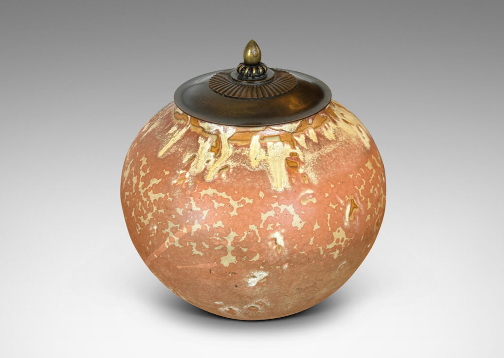 Gallery BAC apered globe form in a marvelous light tan over terra cotta glazing, with bronze patinated lid ornamented with ruffle, coil and finial