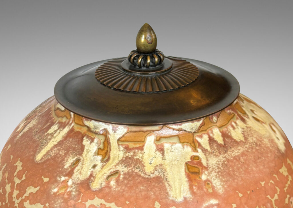 Gallery BAC apered globe form in a marvelous light tan over terra cotta glazing, with bronze patinated lid ornamented with ruffle, coil and finial