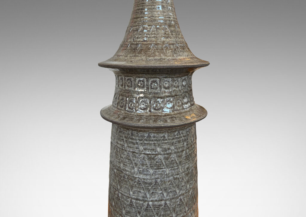 Gallery BAC swelling conical form with flared rings and ornamented with carved zig-zags and impressed rosettes, glazed in a pale warm gray and matte brown