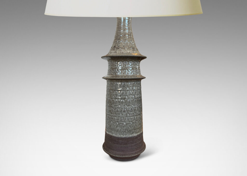 Gallery BAC swelling conical form with flared rings and ornamented with carved zig-zags and impressed rosettes, glazed in a pale warm gray and matte brown