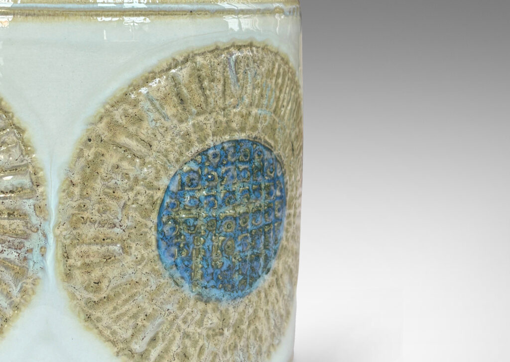 Gallery BAC drum form with relief abstracted floral motifs, glazed in olive-tan and turquoise against a pale gray background