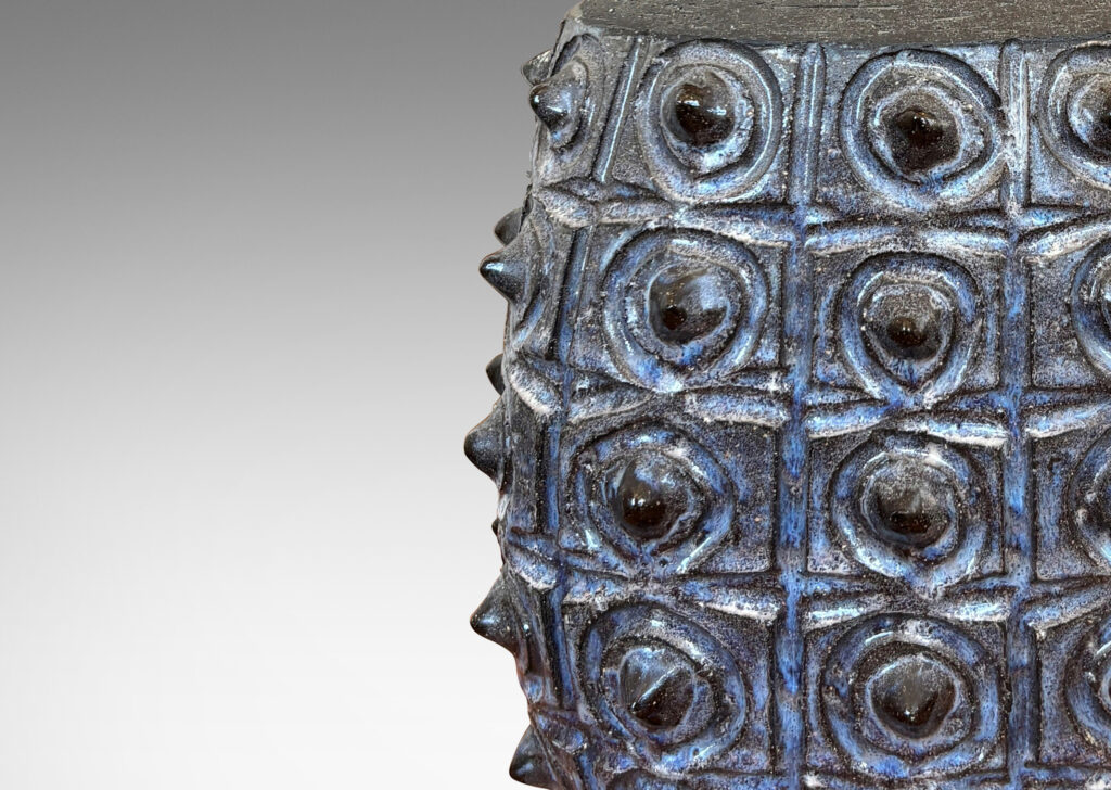 Gallery BAC swelling form with carved design and grid of projecting spines, glazed in pale and dark blue, with sprouting neck in matte brown