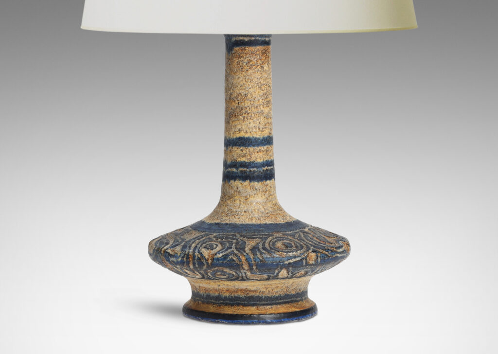 Gallery BAC decanter-like form with low wide body and tall neck, with carved swirling deign, glazed in black against dappled beige-tan