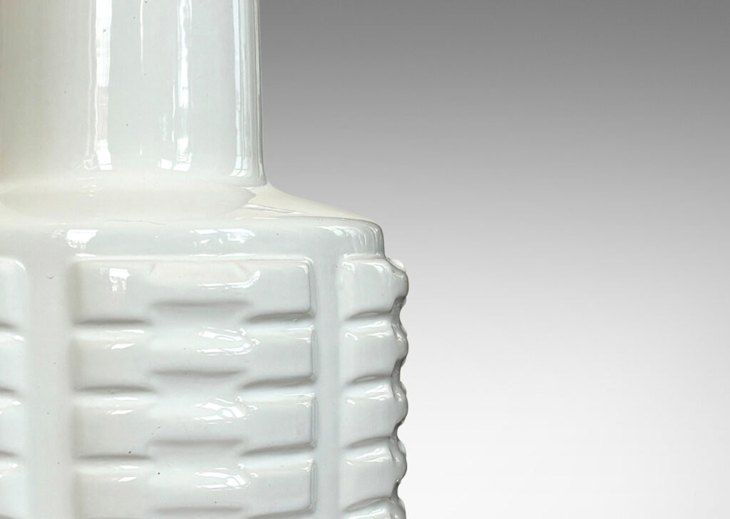 Gallery BAC cylindrical form with stacks of impressed motifs in relief and a tapered neck, glazed in a gloss white