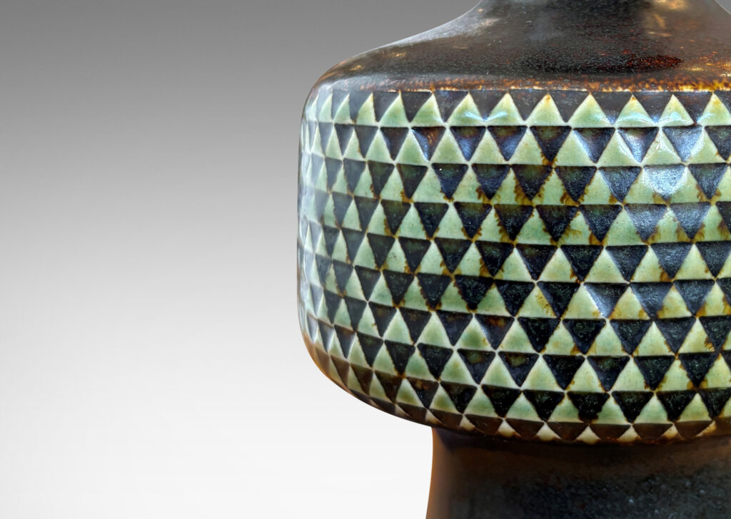 Gallery BAC drum-form fob encircled in impressed triangle motifs floating on a conical base and topped with a sprouting neck, glazed in black and pale gray