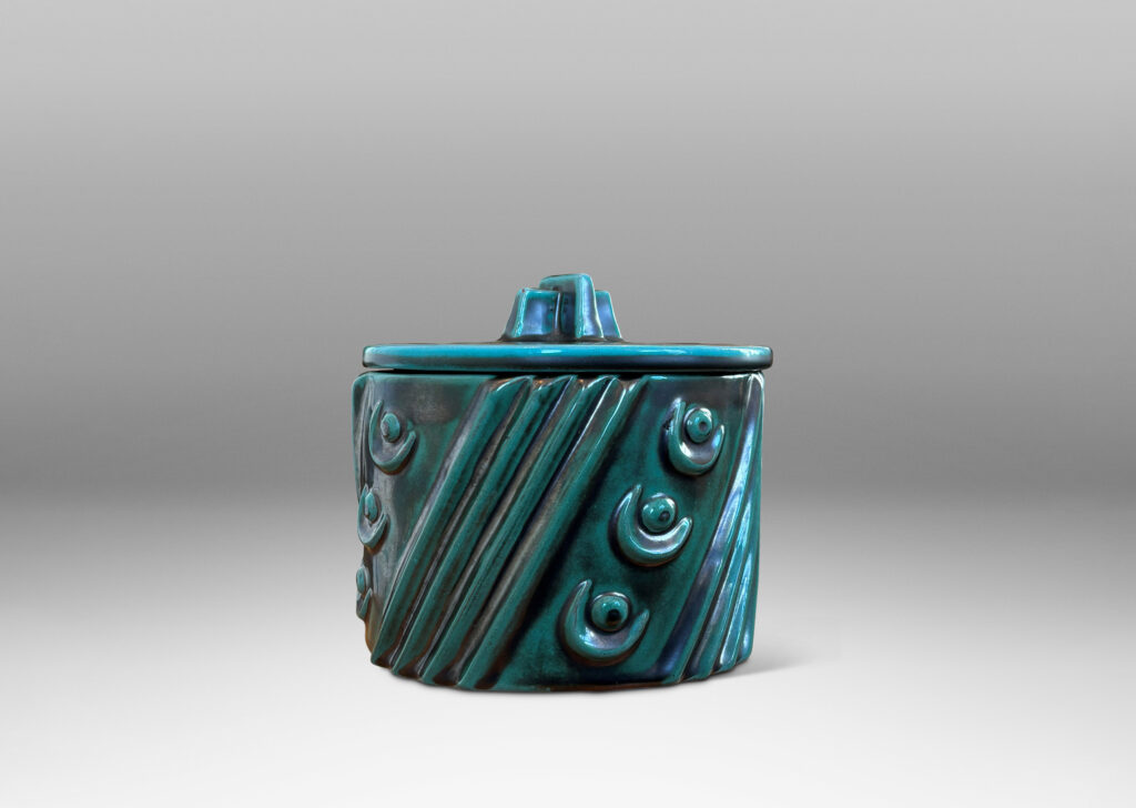 Gallery BAC cylindrical form enlivened with diagonal stripes and motifs in relief, with disk lid top by a cross form final, finished in a tonal teal copper oxide glaze