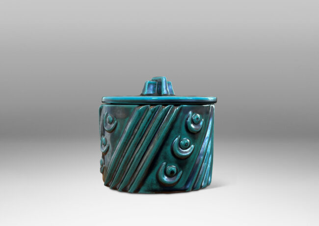 Gallery BAC cylindrical form enlivened with diagonal stripes and motifs in relief, with disk lid top by a cross form final, finished in a tonal teal copper oxide glaze