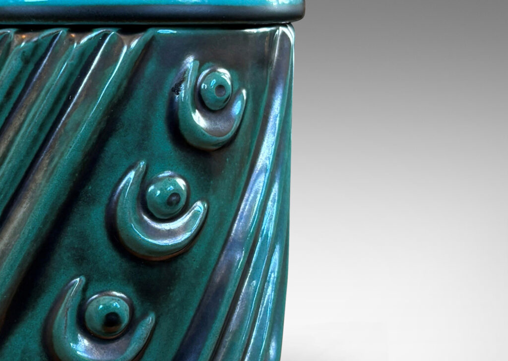 Gallery BAC cylindrical form enlivened with diagonal stripes and motifs in relief, with disk lid top by a cross form final, finished in a tonal teal copper oxide glaze