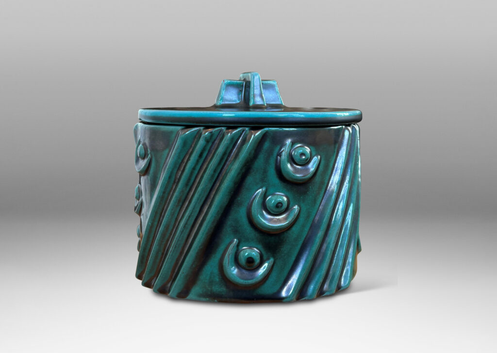Gallery BAC cylindrical form enlivened with diagonal stripes and motifs in relief, with disk lid top by a cross form final, finished in a tonal teal copper oxide glaze