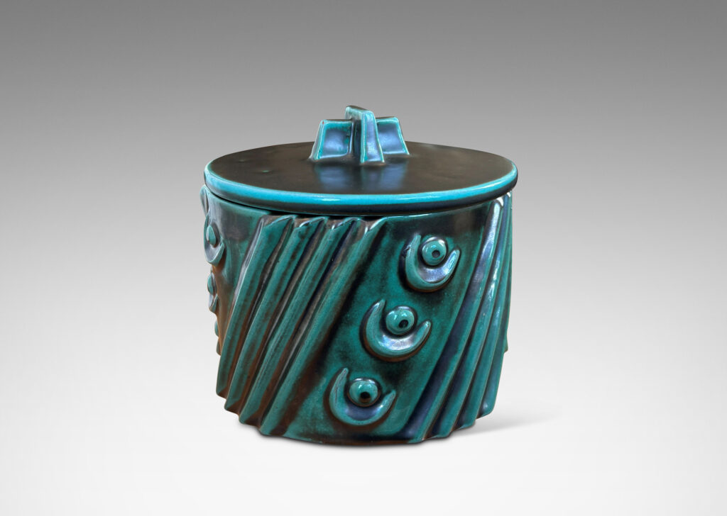 Gallery BAC cylindrical form enlivened with diagonal stripes and motifs in relief, with disk lid top by a cross form final, finished in a tonal teal copper oxide glaze