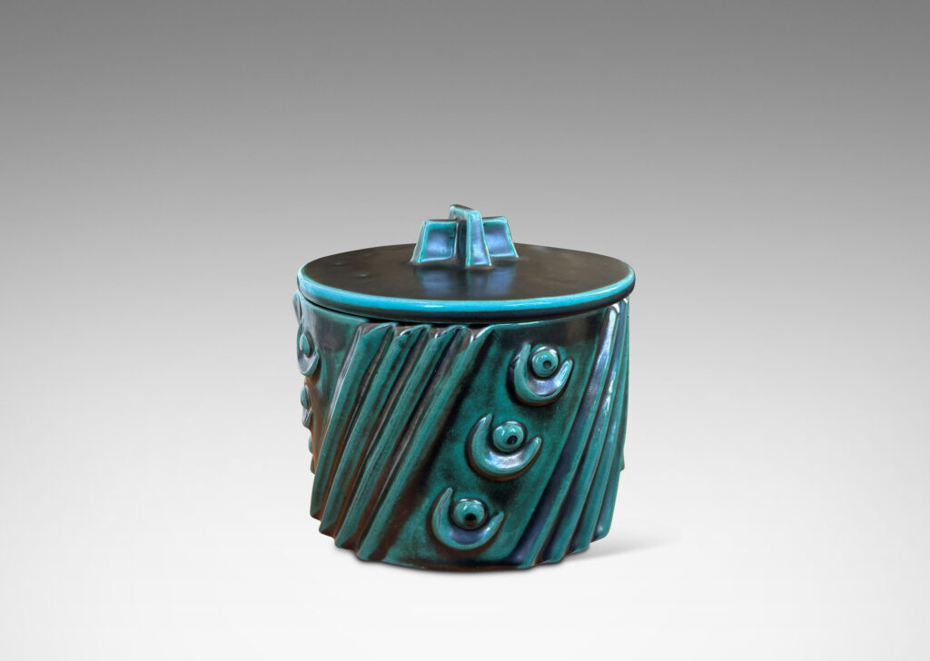 Gallery BAC cylindrical form enlivened with diagonal stripes and motifs in relief, with disk lid top by a cross form final, finished in a tonal teal copper oxide glaze
