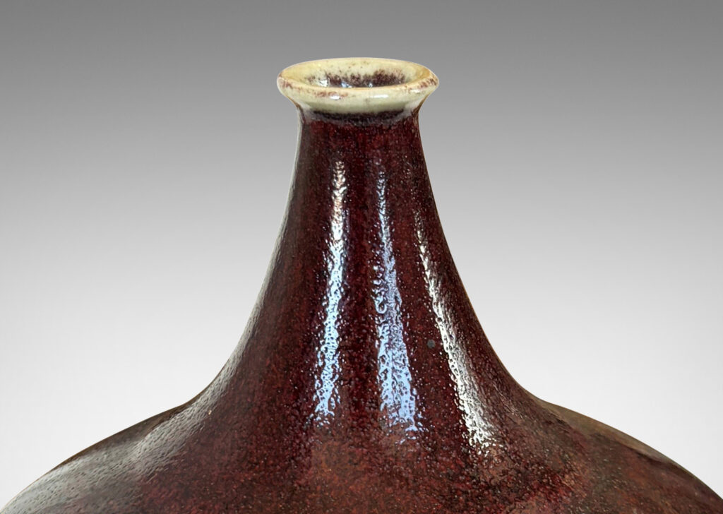 Gallery BAC globe form with straight tapered sides and small sprouted mouth, glazed in a deep burgundy oxblood with pale gray accents