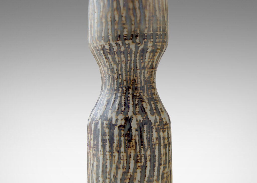 Gallery BAC slender hourglass form with a waist-like cinch and carved texture of diagonal hatches in stoneware with a flowing brown “Birka” glaze