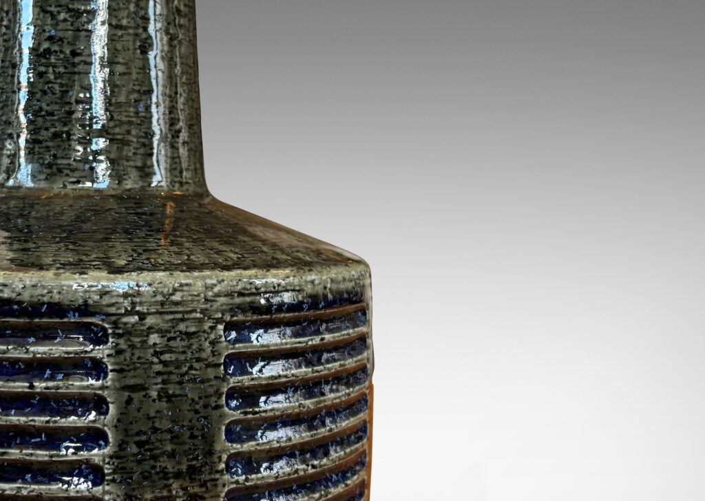 Gallery BAC low drum form with carved score patterning and tall neck, glazed in a shiny gray-green, with blue accents