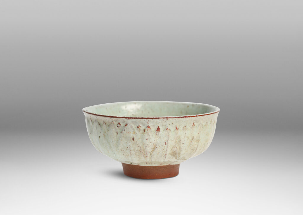 Gallery BAC round form with gently flared lip, on a high reveal, encircled in a relief pattern of overlapping leaves, glazed in a celadon tinted white