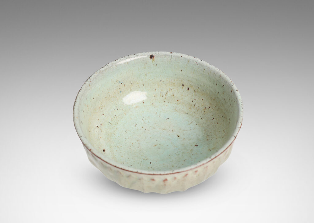 Gallery BAC round form with gently flared lip, on a high reveal, encircled in a relief pattern of overlapping leaves, glazed in a celadon tinted white