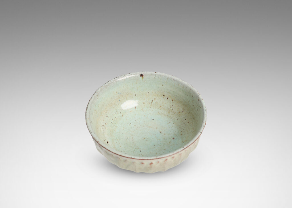 Gallery BAC round form with gently flared lip, on a high reveal, encircled in a relief pattern of overlapping leaves, glazed in a celadon tinted white