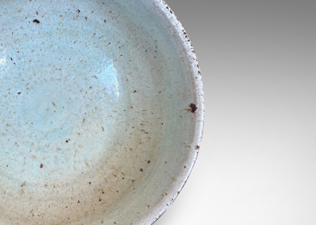 Gallery BAC round form with gently flared lip, on a high reveal, encircled in a relief pattern of overlapping leaves, glazed in a celadon tinted white