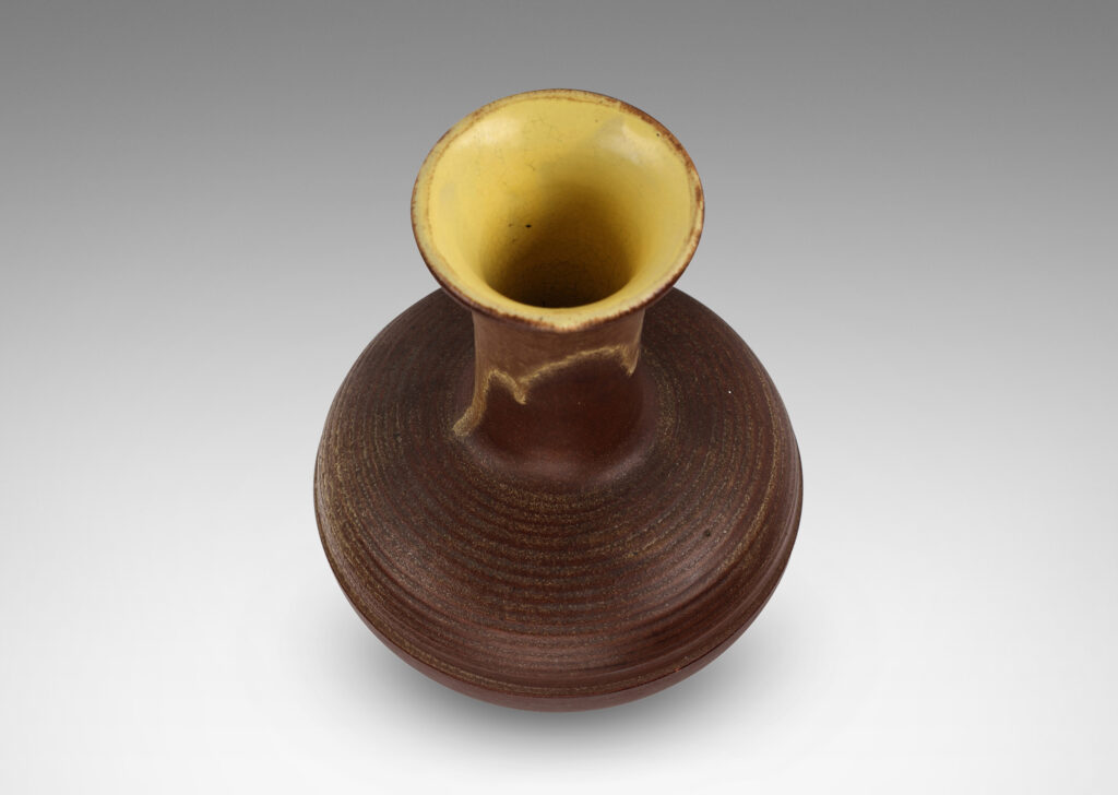 Gallery BAC decanter-like form, with ridged compressed globe body and tall neck with flared mouth, glazed in matte brown with butter yellow interior