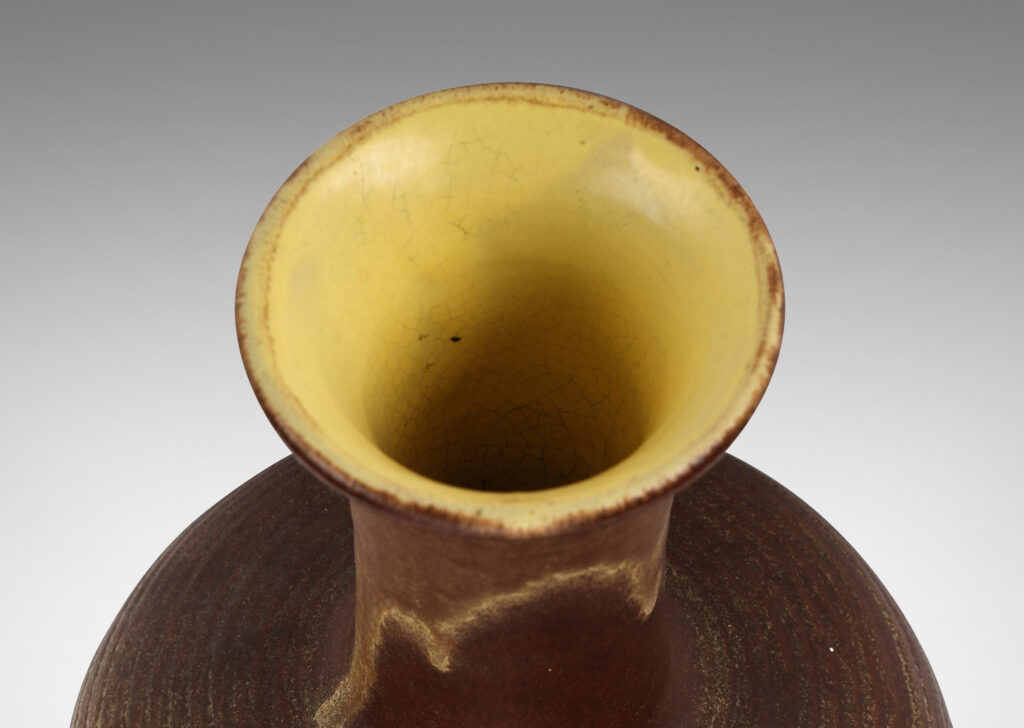 Gallery BAC decanter-like form, with ridged compressed globe body and tall neck with flared mouth, glazed in matte brown with butter yellow interior