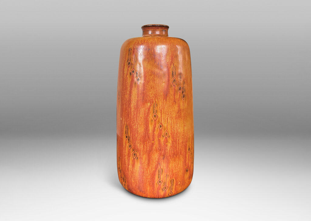 Gallery BAC upwardly tapered cylindrical form with sprouting mouth and floating carved geometric motifs, glazed in a flowing tan-burnt umber