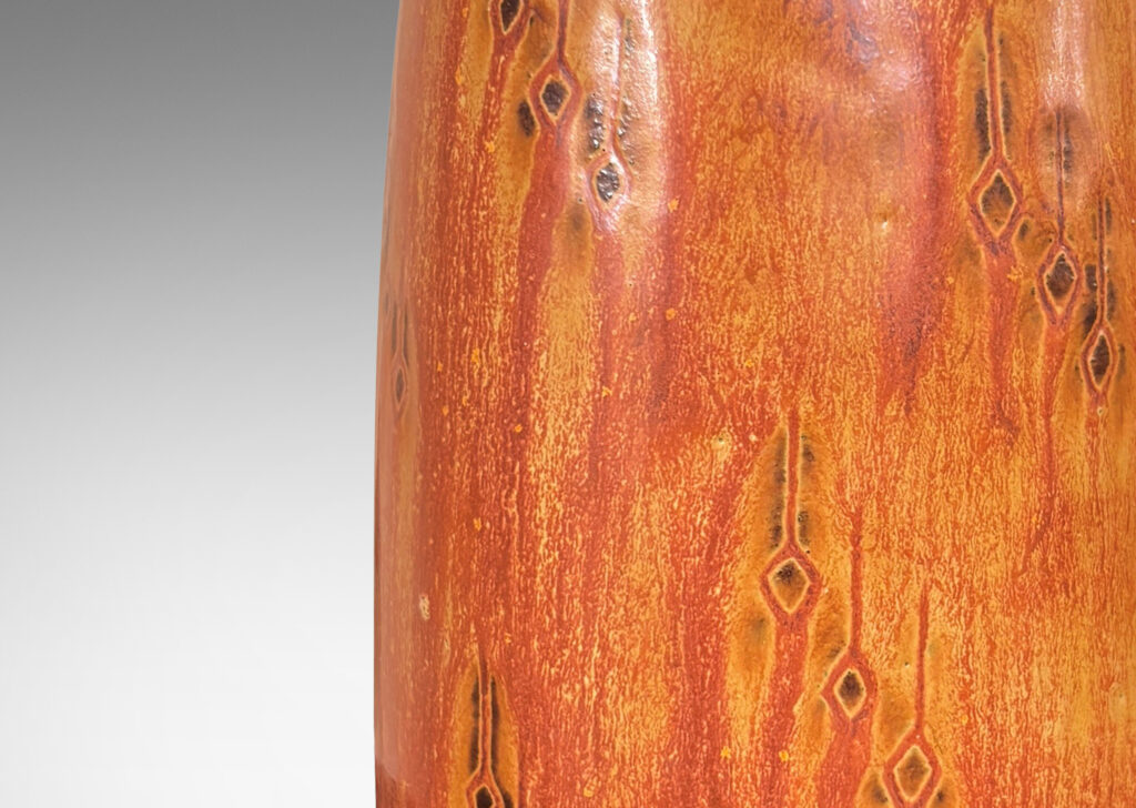 Gallery BAC upwardly tapered cylindrical form with sprouting mouth and floating carved geometric motifs, glazed in a flowing tan-burnt umber