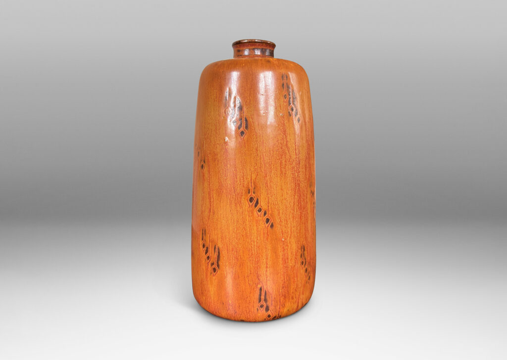 Gallery BAC upwardly tapered cylindrical form with sprouting mouth and floating carved geometric motifs, glazed in a flowing tan-burnt umber