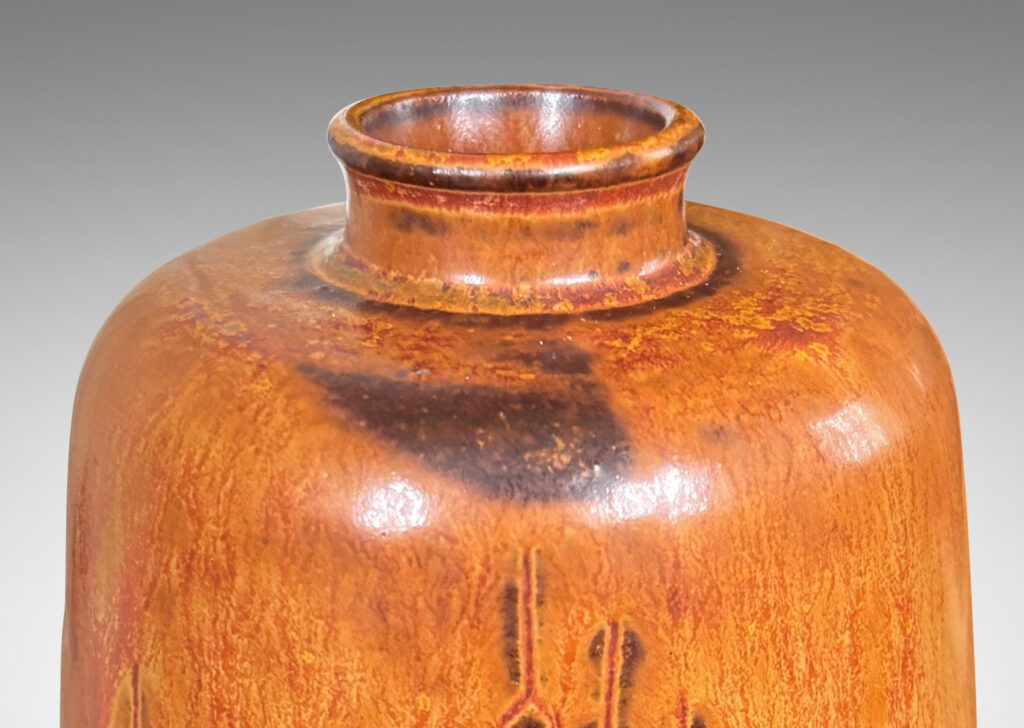 Gallery BAC upwardly tapered cylindrical form with sprouting mouth and floating carved geometric motifs, glazed in a flowing tan-burnt umber
